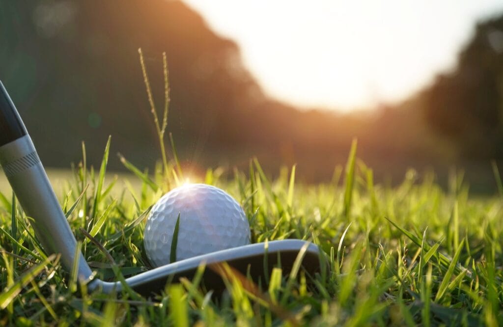 Unscharfer Golfschläger und Golfball in Nahaufnahme im Grasfeld mit Sonne